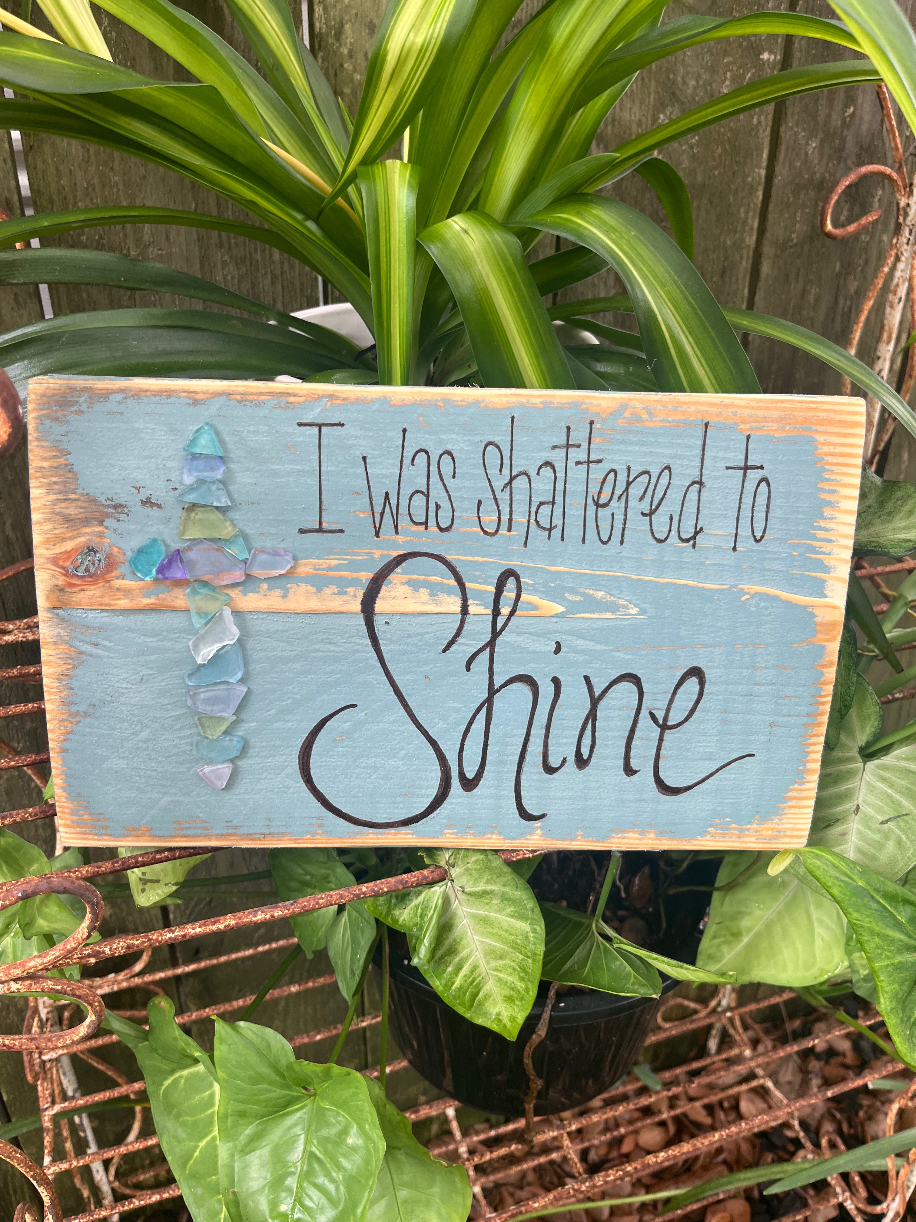 Wooden sign with 'I Was Shattered to Shine' text with glass art in the shape of a cross